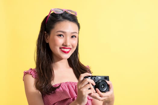 Portrait of a beautiful young asian woman on yellow background with a camera in  hands