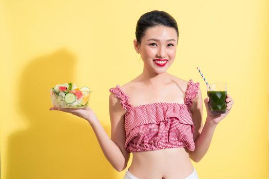 Fashion portrait of young fashionable woman in summer outfit posing with fresh detox smoothie cocktail and salad