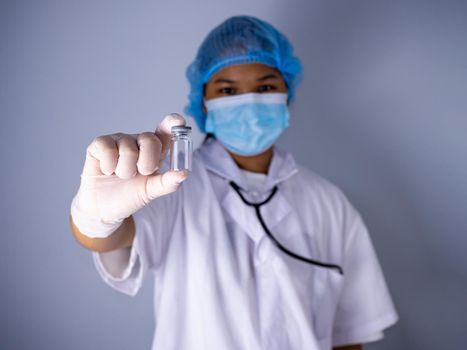 Studio portrait of a female doctor wearing a mask and wearing a hat. in the hand of the vaccine bottle and stretched out his arms in front standing on a white background. studio shot background, COVID-19 concept