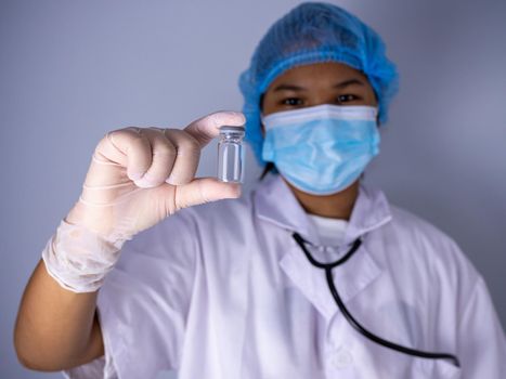 Studio portrait of a female doctor wearing a mask and wearing a hat. in the hand of the vaccine bottle and stretched out his arms in front standing on a white background. studio shot background, COVID-19 concept