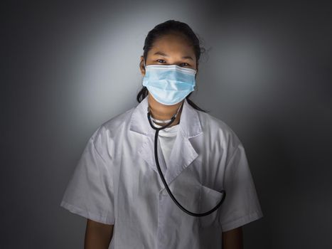 Studio portrait of a female doctor wearing a mask standing on a gray background There was a slight light on his face.