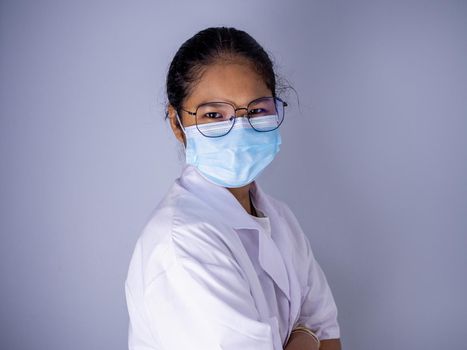 Portrait of a female doctor wearing a mask and wearing glasses standing with arms crossed on a white background