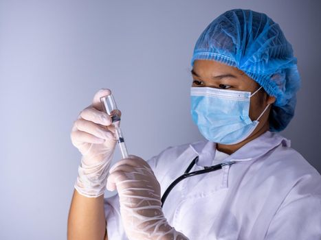 Studio portrait of a female doctor wearing a mask and wearing a hat. In hand was a bottle of vaccine and a sling of syringes. standing on a white background. Studio shot background, COVID-19 concept