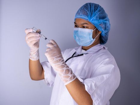 Studio portrait of a female doctor wearing a mask and wearing a hat. In hand was a bottle of vaccine and a sling of syringes. standing on a white background. Studio shot background, COVID-19 concept