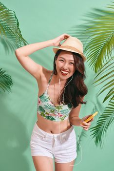 Portrait of happily Asian woman wearing summer clothes and listening to music on the blue background 
