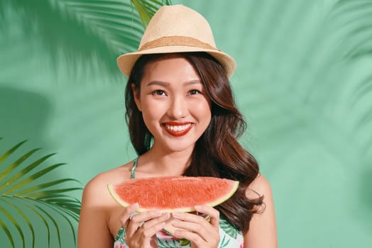 Slice of summer goodness. Beautiful young woman holding slice of watermelon and smiling while standing on blue background