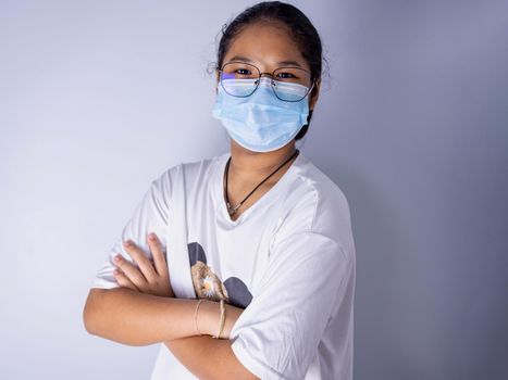 girl wearing a mask and wearing glasses standing with arms crossed on a white background