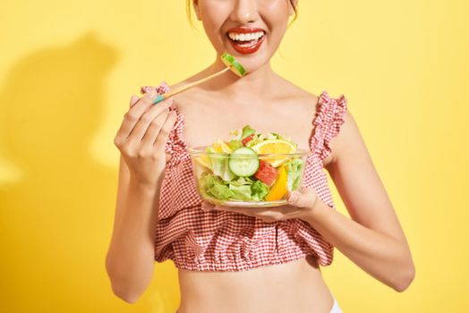 Young woman eating a vegetable salad on yellow background