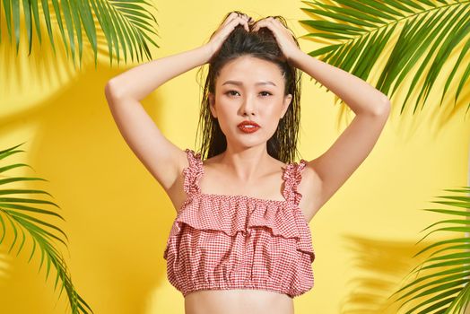 A asia girl with wet hair stands among palm leaves in yellow background