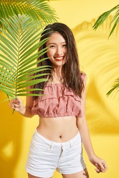 Portrait of Asia Woman holding palm leaf on yellow background