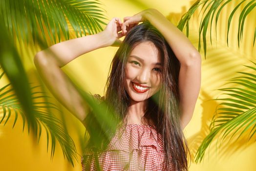 A beautiful girl with wet hair stands among palm leaves in yellow background
