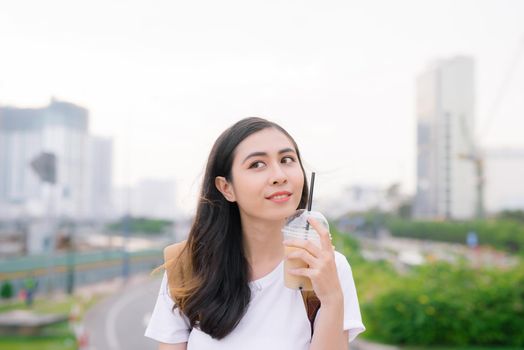 Young beautiful girl standing on a bridge with city view with coffee cup in her hand.