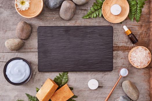beauty product samples and bath salt with evergreen leaves and black stone on  wood table