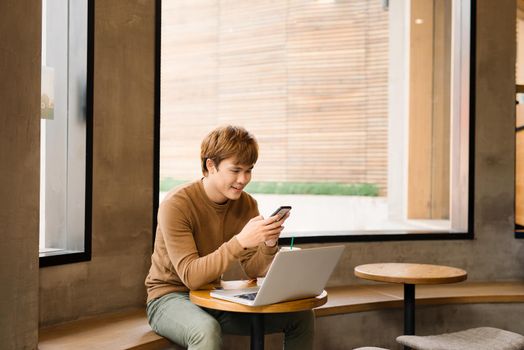 Handsome hipster man receive messages from friend texting answer while chatting through application on smartphone connected to free 5G wireless, male photographer using gadgets in cozy coffee shop