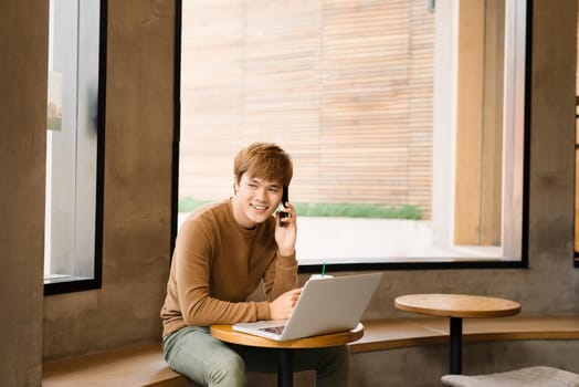 Handsome young business man, talking on the phone while a enjoying the cup of coffee in cafe