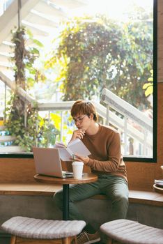 Handsome asian man using laptop sitting on wooden table in coffee shop with a cup of coffee