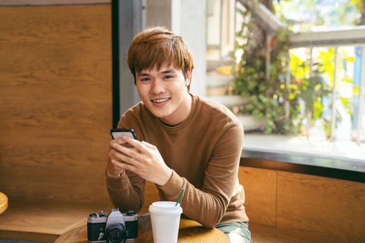 Young Asian man using smart phone during having breakfast, coffee time and summer holiday vacation concepts