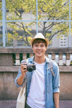 Enjoying travel. Young smiling man with backpack holding camera on asian street.