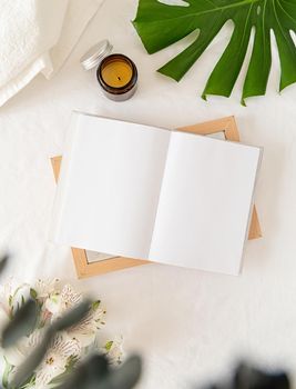 Blank opened book, candle, flowers on white bed, flat lay, mock up, flat lay