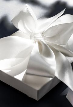 Anniversary celebration, shop sale promotion and luxe surprise concept - Luxury holiday white gift box with silk ribbon and bow on black background, luxe wedding or birthday present