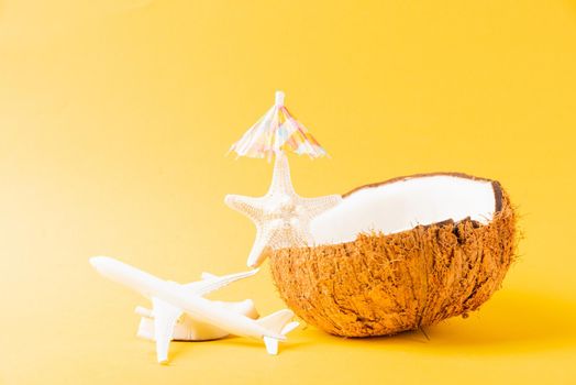 Happy coconuts day concept, fresh coconut, starfish, plane, airplane and sun umbrella, studio shot isolated on yellow background, Beach tropical fruit trip journey and spring summer holiday