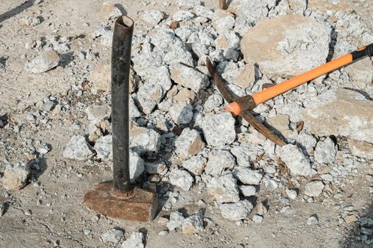 Geological pick with orange handle on the stones next to old hammer.