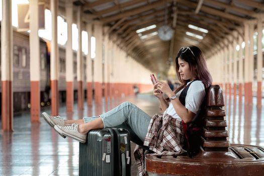 Asian woman is traveler, she is waiting for their train. Girl using smartphone at outdoor adventure travel by train concept.