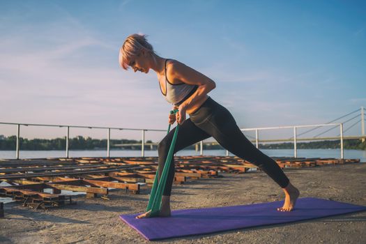 Woman exercising pilates with elastic band on sunny day.