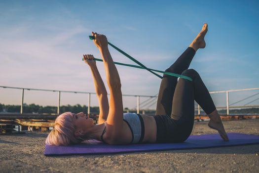 Woman exercising pilates with elastic band on sunny day.