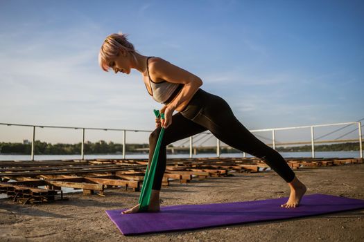 Woman exercising pilates with elastic band on sunny day.