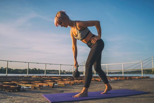 Woman practicing kettlebell pilates on sunny day.