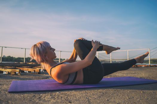 Woman exercising pilates on sunny day. Single straight leg stretch exercise.