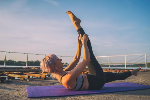 Woman exercising pilates on sunny day. Single straight leg stretch exercise.