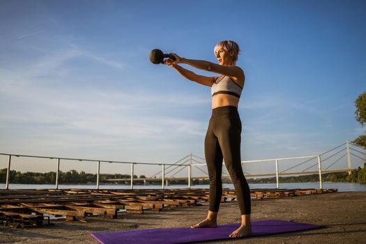 Woman practicing kettlebell pilates on sunny day.