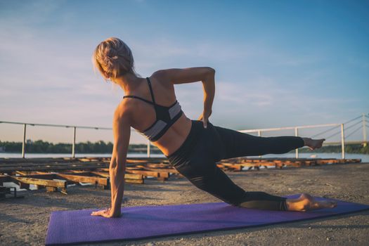 Woman exercising pilates on sunny day. Side plank with leg kick exercise.