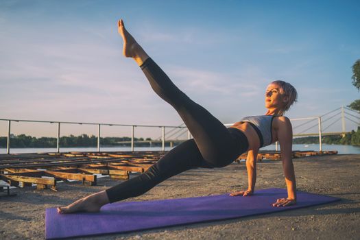 Woman exercising pilates on sunny day. Leg pull back exercise.