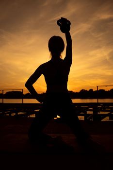 Woman exercising pilates with kettlebell in sunset.