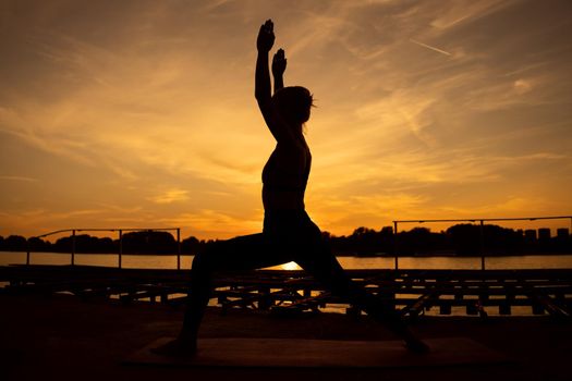 Woman practicing yoga in sunset. Virabhadrasana / Warrior pose