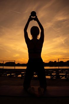 Woman exercising pilates with kettlebell in sunset.