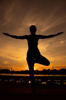 Woman practicing yoga in sunset. Vriksasana, Tree pose