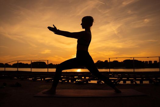 Woman practicing yoga in sunset. Virabhadrasana / Warrior pose