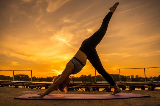 Woman practicing yoga in sunset. Eka Pada Adho Mukha Svanasana/One-Legged Downward-Facing Dog Pose