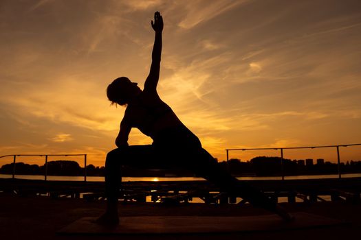 Woman practicing yoga in sunset. Virabhadrasana, Rotated warrior pose