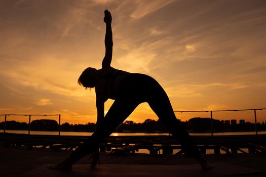Woman practicing yoga in sunset. Trikonasana, Bikram triangle left