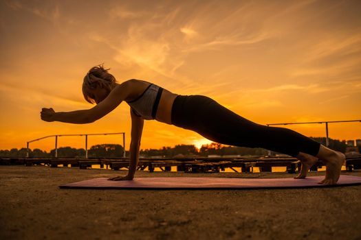 Woman exercising pilates in sunset. One arm ladies push up exercise.