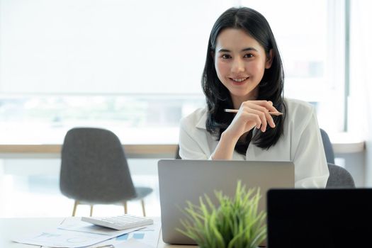 Happy young asian girl working at a her office with a laptop and calculator. Portrait of businesswoman look at camera.