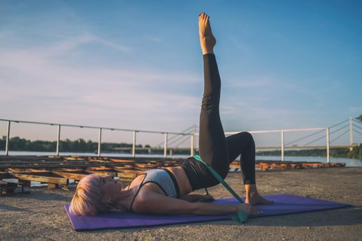 Woman exercising pilates with elastic band on sunny day.