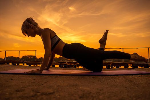 Woman exercising pilates in sunset. One legged ladies push up exercise.