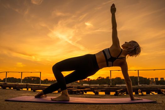 Woman exercising pilates in sunset. Side plank exercise.