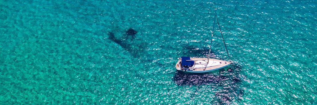 Yacht anchoring in crystal clear turquoise water in front of the tropical island, alternative lifestyle, living on a boat. Aerial view of yacht at anchor on turquoise water, showing luxury, wealth.